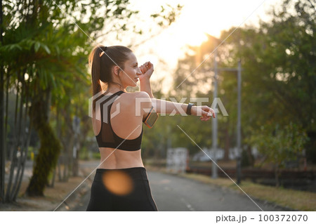 Sporty woman stretching her arms against nature view at sunny morning background. Fitness, sport and healthy lifestyle concept 100372070