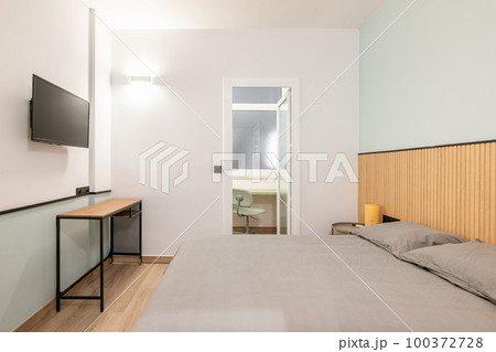 Compact stylish bedroom in stylish soothing colors with a double bed, TV with access to closed balcony with an office area. Concept of a small cozy bedroom of young family. 100372728