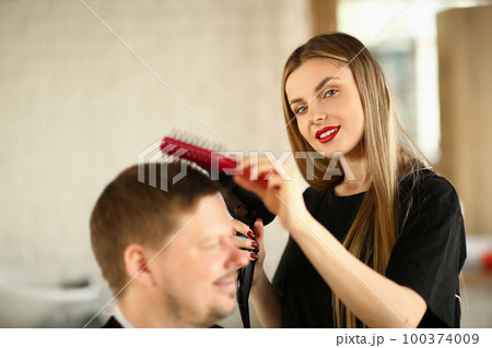 Woman in hairdresser hairdresser makes ahairstyle with hair dryer for male client 100374009