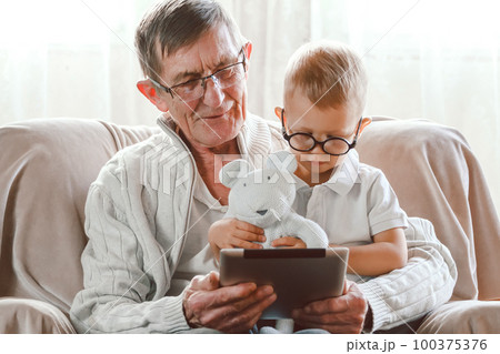 Elderly grandfather and his little grandson use a tablet device together 100375376