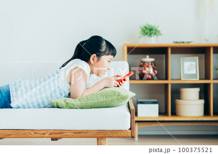 リビングでスマホを見る小学生の女の子 100375521