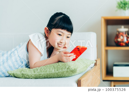 リビングでスマホを見る小学生の女の子 100375526