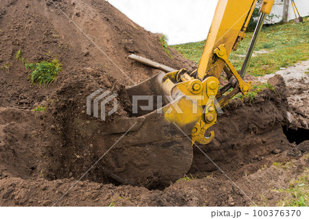 A bucket of excavator or bulldozer with a pile of earth digs a hole on the construction site close up A bucket of excavator or bulldozer with a pile of earth digs a hole on the construction site close up 100376370