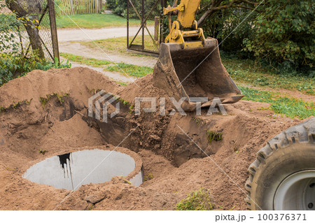 A bucket of excavator with a pile of sand and earth buries sewer concrete rings in the industrial zone 100376371