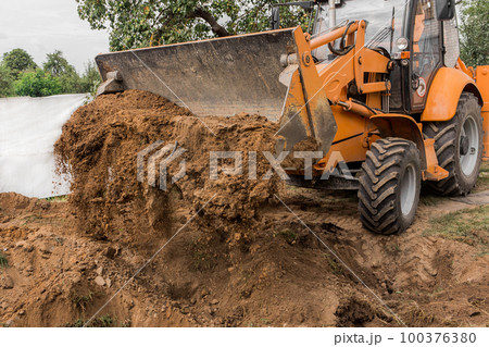 A bucket of a bulldozer fills the trench with earth in an industrial zone. Excavation construction works 100376380