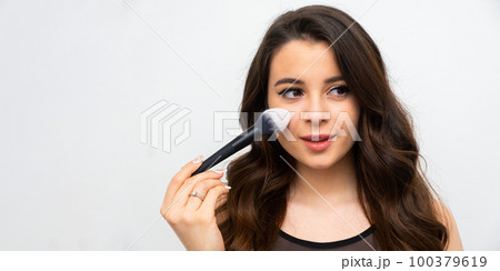 Beautiful makeup artist applies powder on cheek on the white background with copy space.  100379619