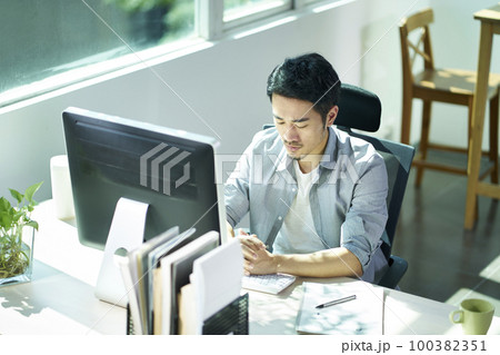 young asian business man entrepreneur sitting at desk in office contemplating 100382351