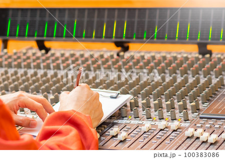male songwriter hand writing a song on audio mixing console in recording studio. songwriting concept 100383086