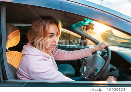 A young woman sits behind the wheel of a right-handed car and looks in the rear-view mirror. A young woman sits behind the wheel of a right-handed car and looks in the rear-view mirror. 100391254