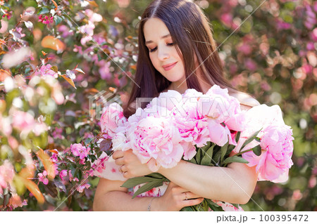A happy beautiful girl holding a large bouquet of pink peonies A happy beautiful girl holding a large bouquet of pink peonies 100395472