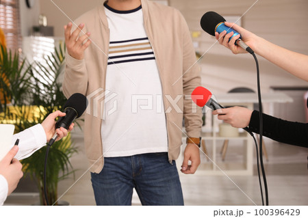 Group of journalists interviewing man in room, closeup 100396429