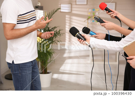 Group of journalists interviewing man in room, closeup 100396430