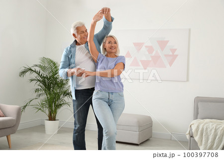 Happy mature couple dancing together in living room Happy mature couple dancing together in living room 100397708