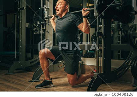 Fit man doing squats in a training machine 100400126