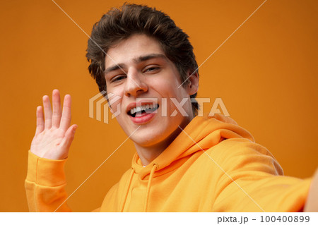 Young handsome man wearing casual hoodie waiving saying hello on yellow background 100400899