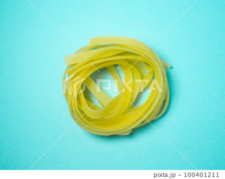 Nests of pasta on a blue background.   Culinary background. Pyramid of noodles. Curled pasta on the table. Uncooked product.  Background from noodles. 100401211