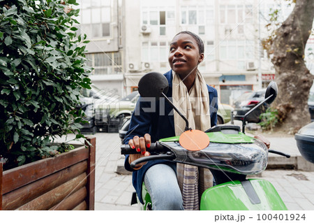 Portrait of a young and stylish african woman with a moped in the city 100401924