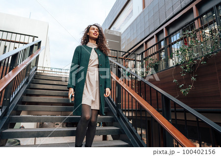 Portrait of young woman in green coat with curly hair in the city 100402156