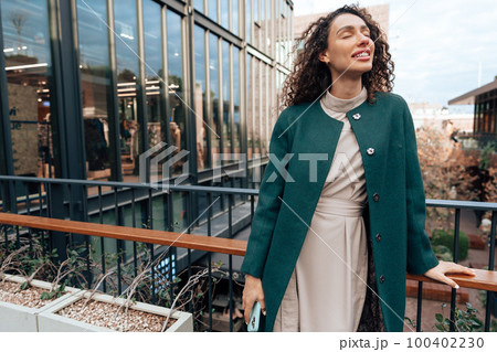 Portrait of young woman in green coat with curly hair in the city Portrait of young woman in green coat with curly hair in the city 100402230