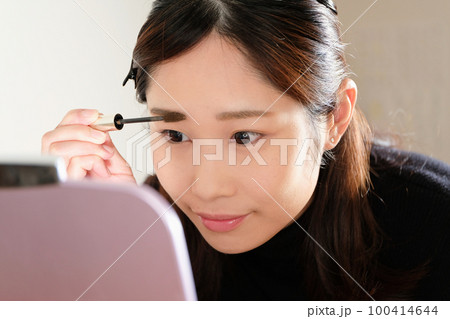 鏡を見ながら眉毛を描く女性のクローズアップ 100414644