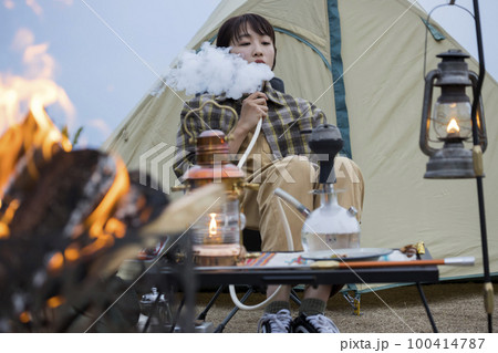 夕方、焚火をしながらで水タバコを吸う若い女性 シーシャ 夕方、焚火をしながらで水タバコを吸う若い女性 シーシャ 100414787