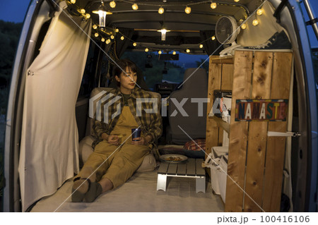 夜のオートキャンプ場で車の中で寛ぐ若い女性　車中泊イメージ 100416106