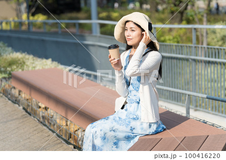 公園でテイクアウトコーヒーを飲む若い女性 100416220