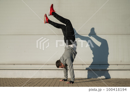 Caucasian man in hooded sweatshirt doing handstand outdoors.  100418194