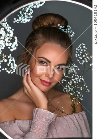 Portrait of a smiling beautiful, sweet girl on a gray background with white flowers. 100419142