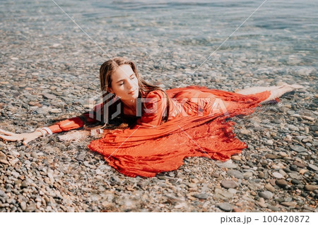 Woman travel sea. Happy tourist in red dress enjoy taking picture outdoors for memories. Woman traveler posing in sea beach, surrounded by volcanic mountains, sharing travel adventure journey Woman travel sea. Happy tourist in red dress enjoy taking picture outdoors for memories. Woman traveler posing in sea beach, surrounded by volcanic mountains, sharing travel adventure journey 100420872