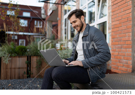 businessman holding an online meeting remotely sitting in a laptop on the street 100421573