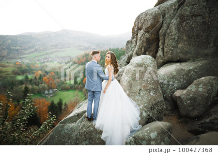 Beautiful gorgeous bride posing to groom and having fun near at mountains with amazing view, space for text, wedding couple 100427368