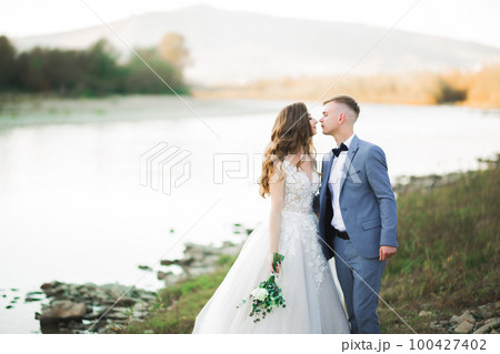 Elegant stylish happy blonde bride and gorgeous groom on the background of a beautiful river in the mountains Elegant stylish happy blonde bride and gorgeous groom on the background of a beautiful river in the mountains 100427402