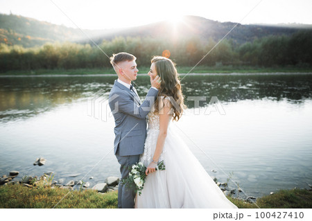 Elegant stylish happy blonde bride and gorgeous groom on the background of a beautiful river in the mountains 100427410