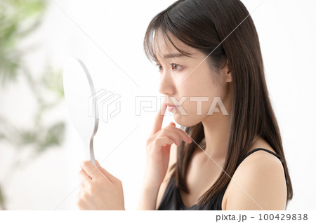 鏡で心配そうに顔を確認する女性 100429838