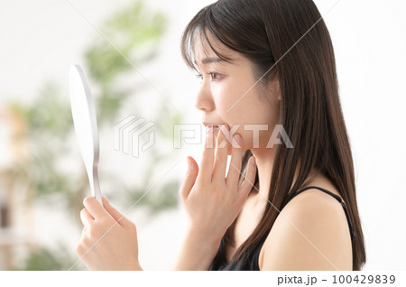 鏡で心配そうに顔を確認する女性 100429839