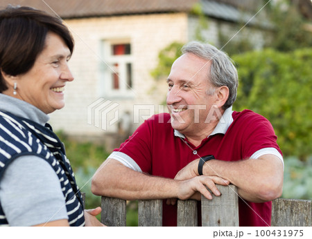 Positive mature man and woman standing near fence in garden Positive mature man and woman standing near fence in garden 100431975