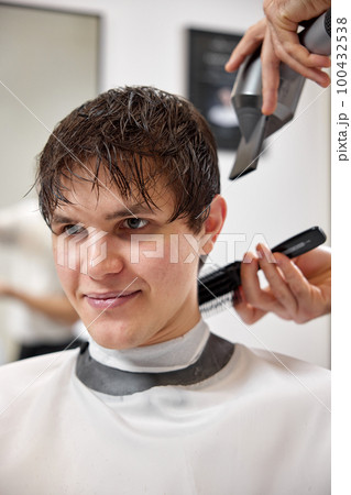 Professional hairdresser during work with man client with hair dryer in barber shop. Haircut in the barbershop. Professional hairdresser during work with man client with hair dryer in barber shop. Haircut in the barbershop. 100432538