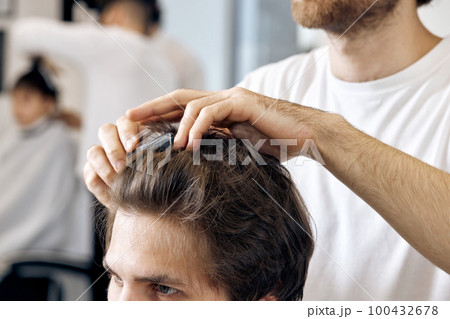 close-up, professional male hairstylist combing young customer's hair 100432678