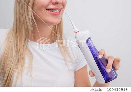 Portrait of a caucasian woman with braces on her teeth holding an irrigator. Portrait of a caucasian woman with braces on her teeth holding an irrigator. 100432913