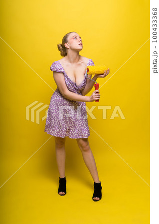 Young classic pin-up woman painting wall with paint roller 100433368