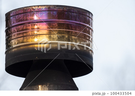 Round shiny metal chimney with heat tint and soot is under blue sky Round shiny metal chimney with heat tint and soot is under blue sky 100433504