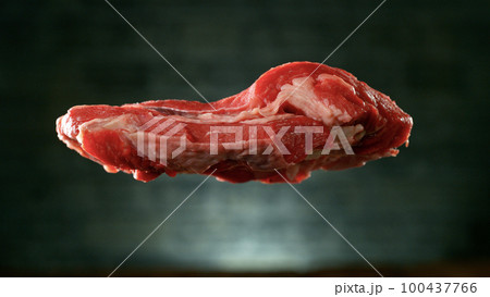 Flying pieces of raw beef steak falling on table, grey brick wall on background. 100437766