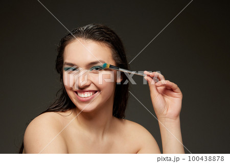 Happy young woman with perfect skin, long brunette shiny hair and beautiful smile posing over grey background. Beauty, skin care, cosmetology, spa, ad concept 100438878