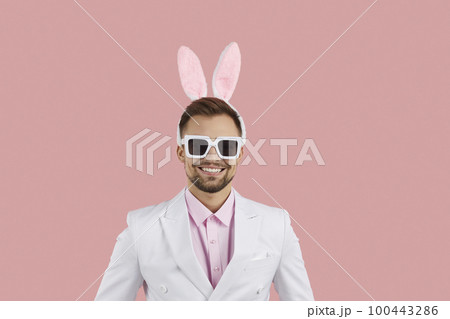 Young happy Caucasian man with funny bunny rabbit ears on head dressed in classic white suit 100443286