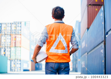 portrait of asian man smiling engineering in uniform holding hardhat standing containers yard. 100443323