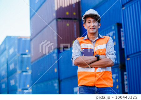 portrait of asian man smiling engineer arm crossed in uniform holding hardhat and tablet. 100443325