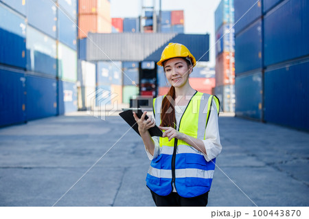 Smiling beautiful female industrial engineer in uniform wearing safety hard hat using tablet. Smiling beautiful female industrial engineer in uniform wearing safety hard hat using tablet. 100443870