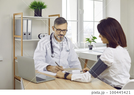 Man doctor gives prescription after checking blood pressure of young woman patient 100445421
