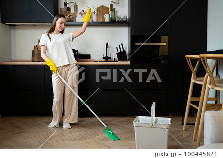 Carefree happy woman cleaning the living room at home is dancing merrily with a mop. Carefree happy woman cleaning the living room at home is dancing merrily with a mop. 100445821